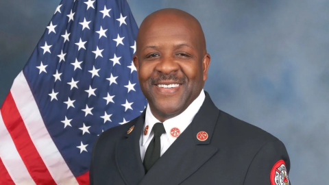 Clayton Farr poses in a suit, holding his fire chief cap on his side.