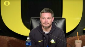Head Oregon Football Coach Dan Lanning sits behind a microphone, ready to answer questions from the press. 