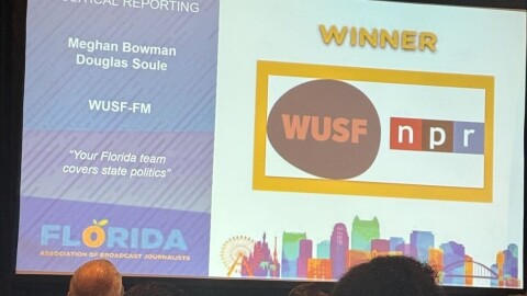 A large screen projects WUSF's logo with the text winner for political reporting Meghan Bowman and Douglas Soule WUSF-FM "Your Florida team covers state politics" 