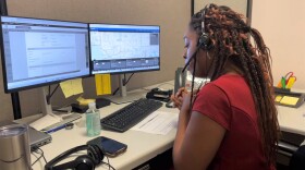 A phone operator fields a call sitting at a cubicle while wearing a black headset. 