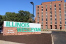 Brick entrance to Illinois Wesleyan University with a row of bushes in front of a sign