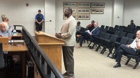 Image of man standing at podium in tan suit. Carrlo Heard is an associate pastor at Omega Baptist Church. He wants police to explain why police shot and killed a 16-year-old on June 29, 2024.