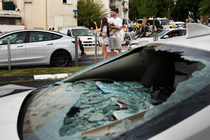 Onlookers stand behind a car that was damaged at the rare rocket strike in Tel Aviv on Friday.