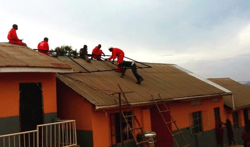Workers installing solar panels on a school, part of All We Are's Solarize Uganda Now (SUN) Project.