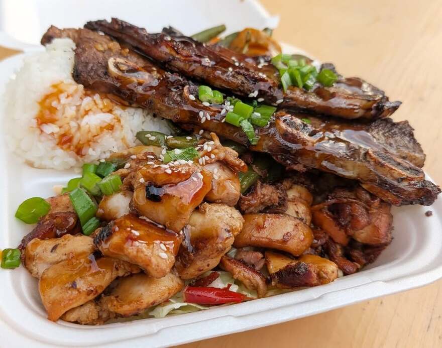 A meal of ribs, rice and vegetables in a take out container.