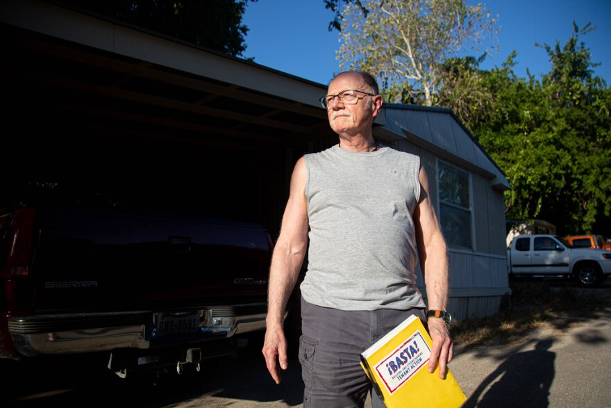 A man stands in a sleeveless gray T-shirt holding a booklet that says BASTA on it.