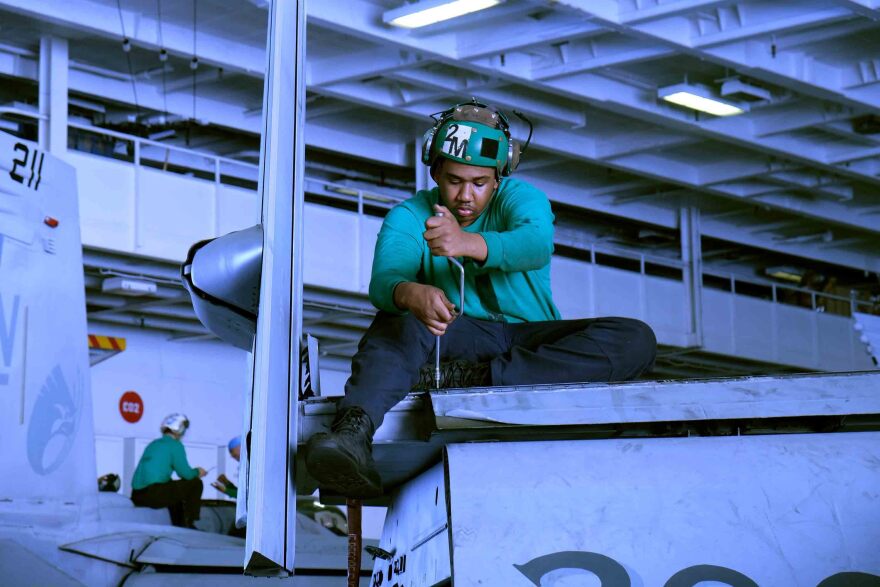 A mechanic works on the wing of a Navy fighter jet in the hangar beneath the flight deck of the USS Carl Vinson.