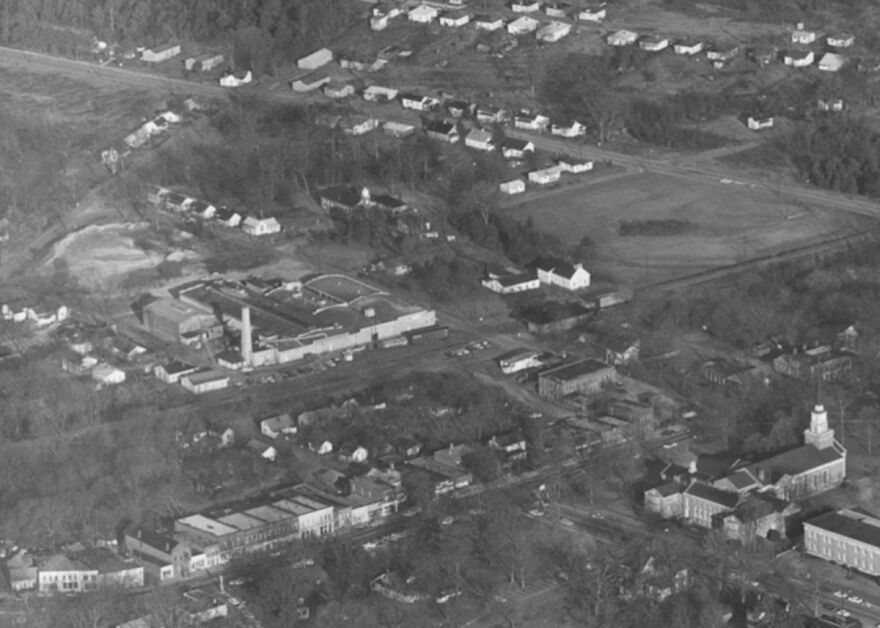 An aerial photo of the Linden Mill, later the Carolina Asbestos Company, with smokestack, in downtown Davidson. Main Street and Davidson College Presbyterian Church are at the bottom. The photo is probably from the 1950s or 1960s.