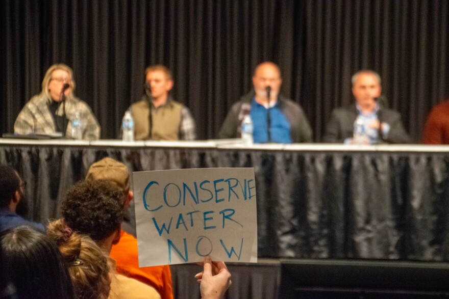 One attendee holds up a sign that says "conserve water now" in front of the panel of Google representatives on Thursday. One representative outlined Google's planned requests for further wetland mitigation credits as well as a plan to relocate Adams Ditch on the property.