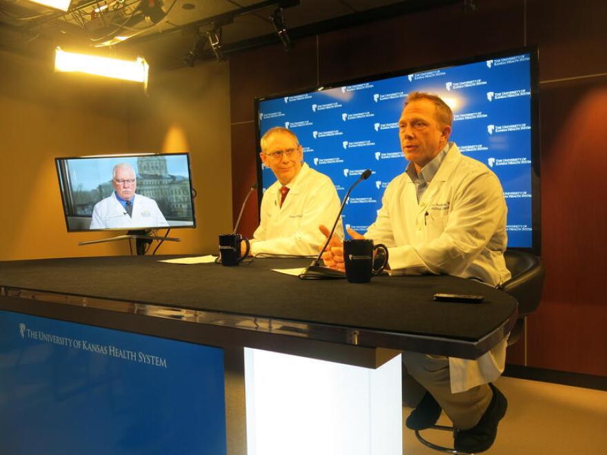 University of Kansas Health System doctors Steven Stites (left) and Dana Hawkinson at a media briefing early in metro Kansas City's coronavirus outbreak. Kansas Health Secretary Lee Norman is on the television monitor.