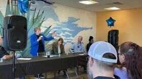 Lady stands, holding microphone, talking to audience