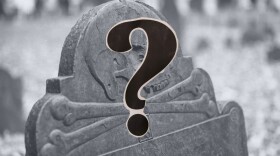An old gravestone with a skull and crossbones on the top; a question mark in the foreground