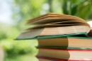 An open book sits on a stack of books on a wooden table in a garden. 