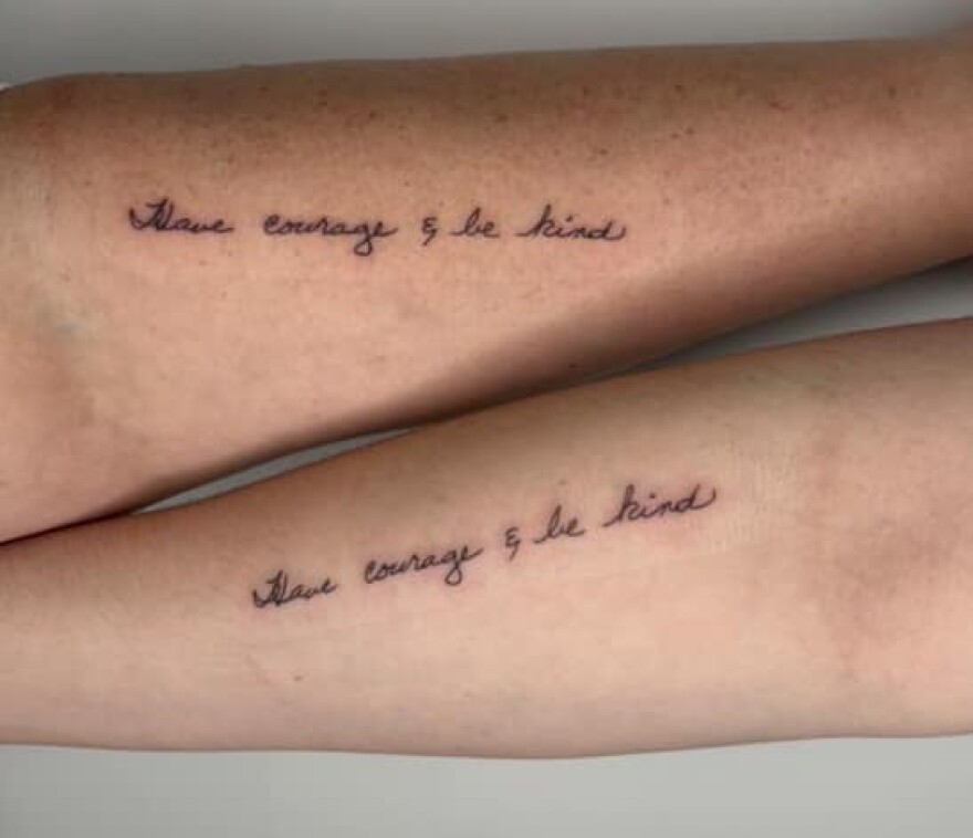 Two forearms displayed with matching tattoos saying "Have courage and be kind."