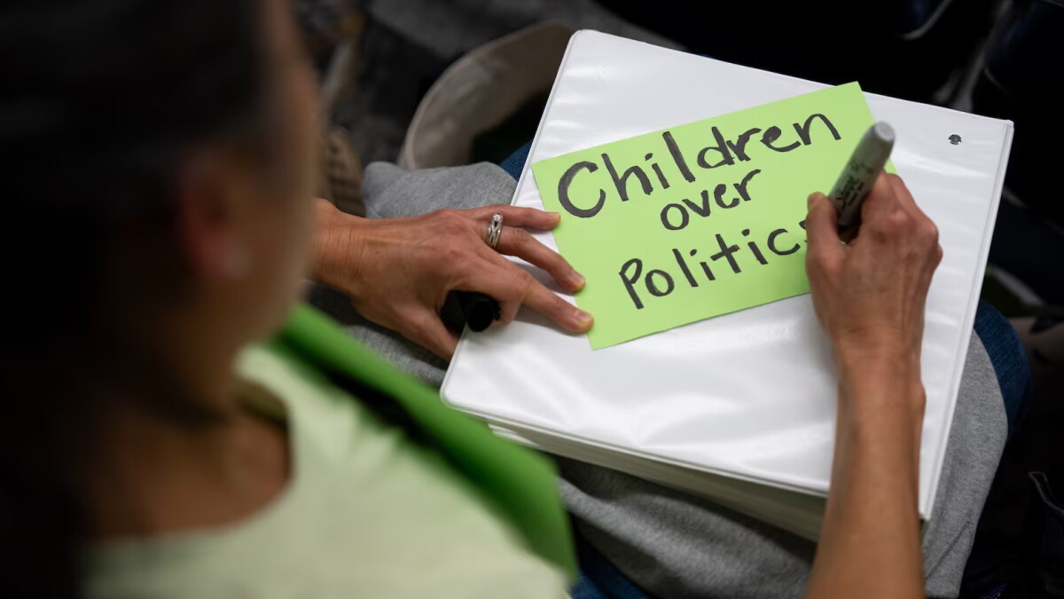 FILE - Kaori Eder, pens "children over politics” on a sign board during a Portland Public Schools board meeting at the Dr. Matthew Prophet Education Center in Portland, Ore., in April 2026.