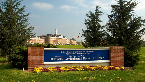 A blue sign reading "Beltsville Agricultural Research Center" sits at the entrance of a research campus, with a large building in the background