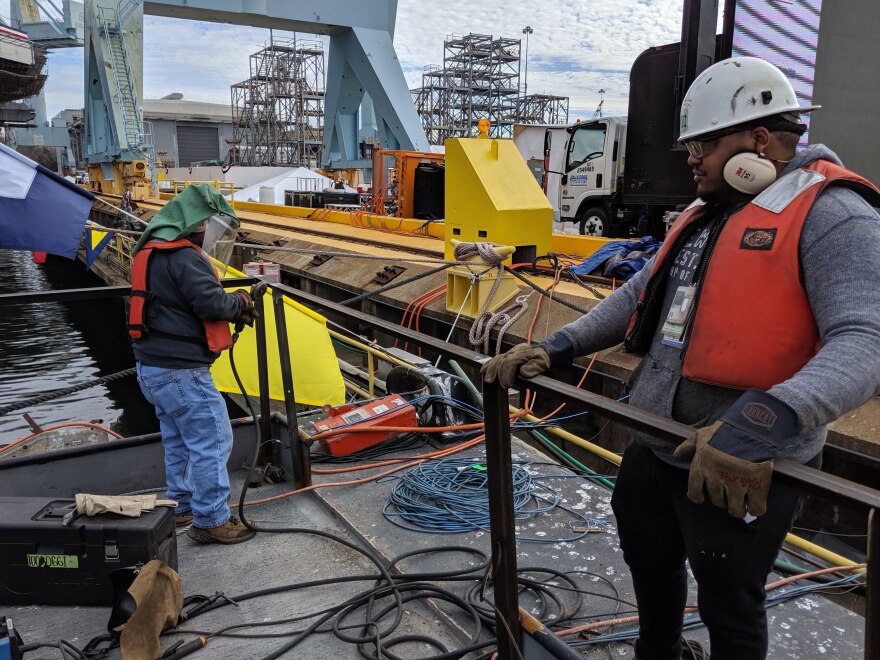 A day before the christening of the USS John F. Kennedy, welders Hector Valencia (left) and Hamilton Haynes (right) with Newport News Shipbuilding smoothed recently welded metal railings near the edge of where thousands will gather to celebrate the event.