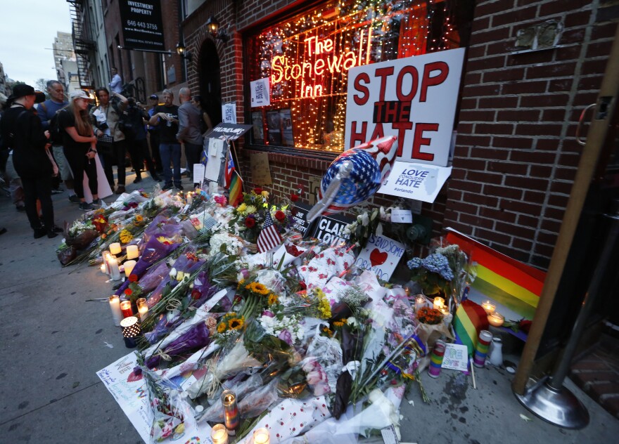 People gather to look at a makeshift memorial for victims of the Orlando nightclub shootings in front of the historic Stonewall Inn, a gay bar in the West Village, on June 13, in New York.