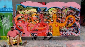 Savonnara Alexander Sok sitting by his freshly painted mural at The Avenue Concept in Providence, RI. Here, the characters are experiencing a non-traditional form of love.