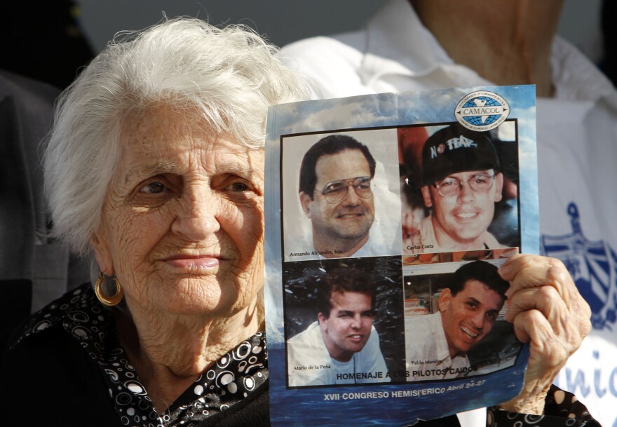 An elderly woman holds a piece of paper with the photos of four men