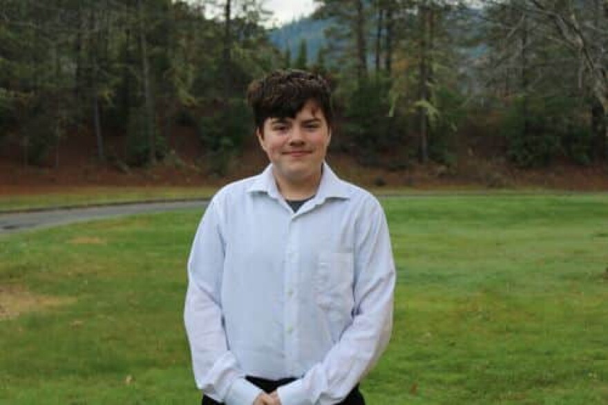 Jaydon Boyle stands on a lawn in a white button-down shirt, with trees behind him.