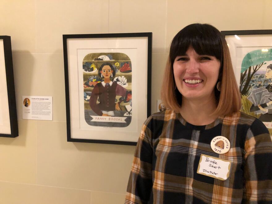 A woman stands in front of framed pictures.
