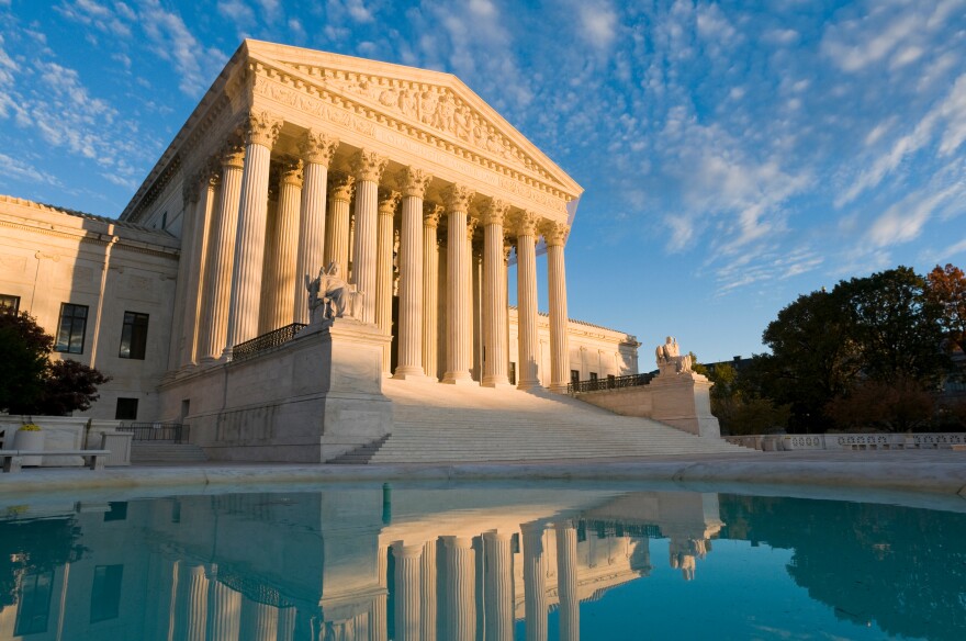 The front of the US Supreme Court in Washington, DC, at dusk. The building is reflected in the ornamental pool.