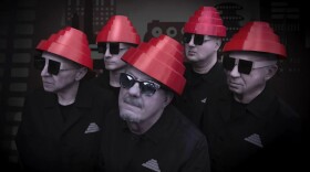 Five men wearing sunglasses, black shirts and red hats in the shape of a cone, tapered toward the top