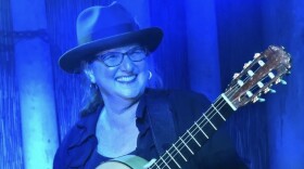 A woman on a blue lit stage performing with an acoustic guitar. 