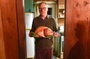 Man with somber expression holding a very large cooked turkey on a platter