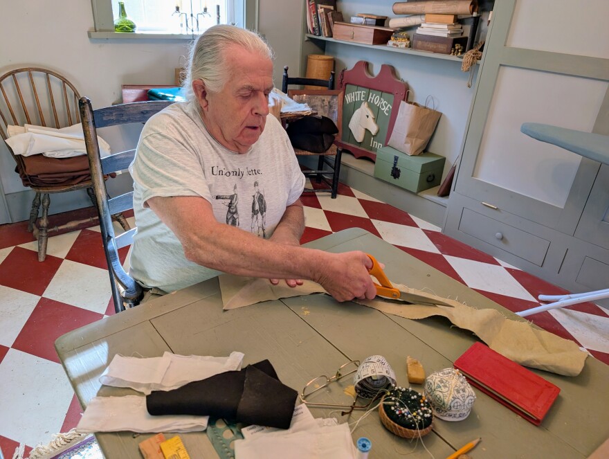 Paul Brennan uses scissors to cut fabric on the table inside his tailor's shop.