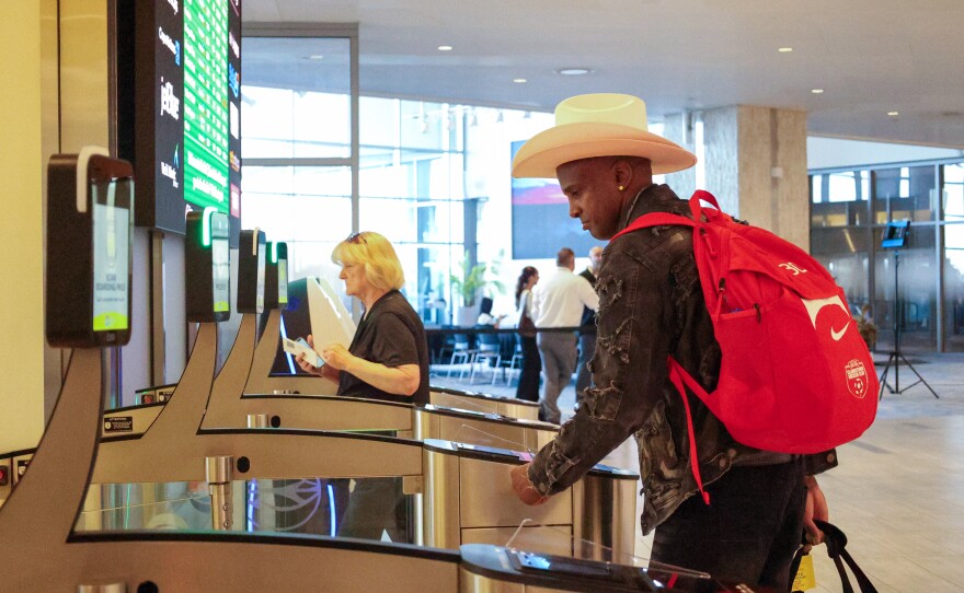 Man in cowboy hat and wearing a backpack walks through an airport security gate.