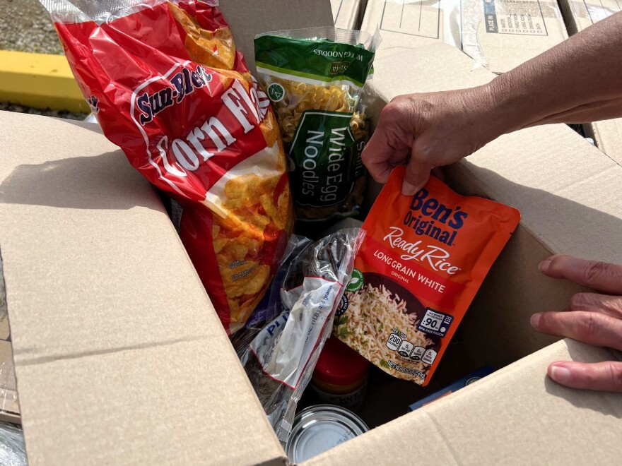 A cardboard box is filled with dry goods like corn flakes, egg noodles and instant rice.