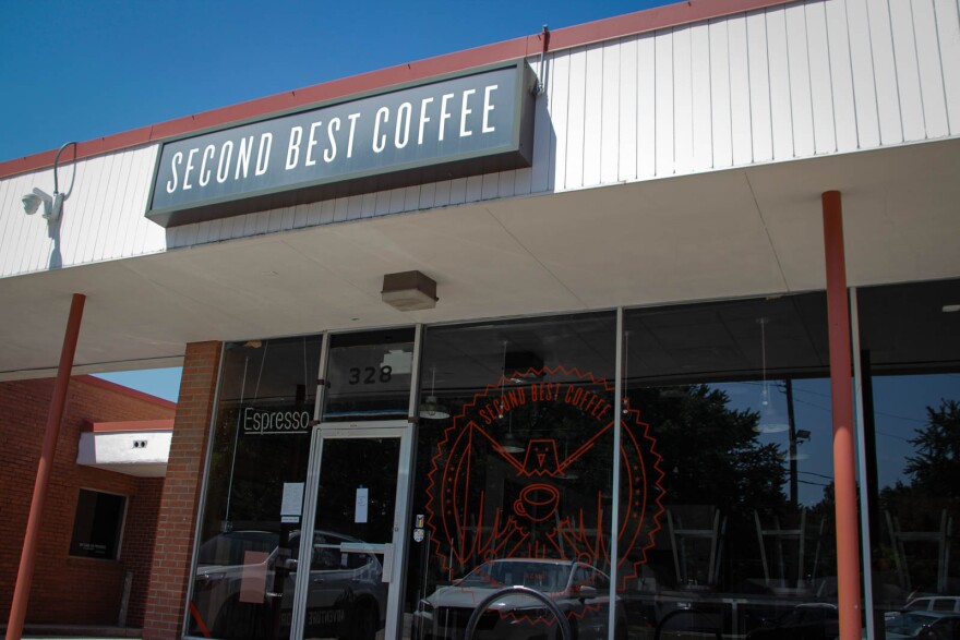 A coffee shop in a strip mall has a graphic on the window of an eagle holding a cup of coffee. The sign reads "Second Best Coffee"