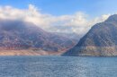 A wide shot of Lake Mead and the surrounding mountains. The sky is blue and clouds are hanging at the mountain peaks. 
