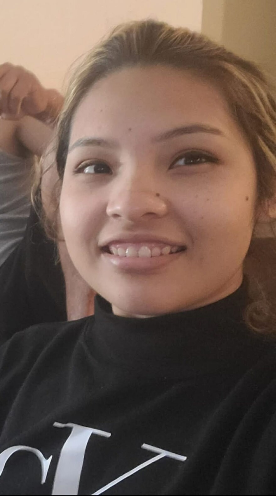 A young woman with brown hair and blonde highlights smiles. She has her hair pulled back and is wearing a black and white turtleneck. 