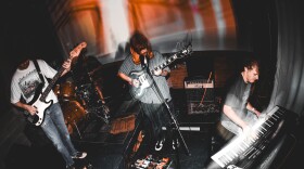 Three people perform on two guitars and a keyboard.