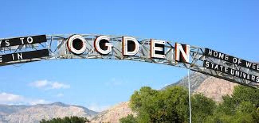 An arch that says "Ogden" hangs above a roadway with mountains in the background.