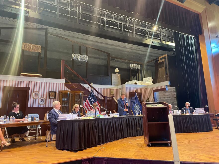 Executive Councilors and Gov. Sununu sit in a theatre at New England College for the meeting.