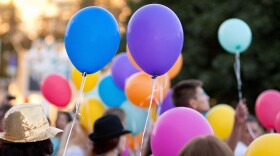 a bunch of people standing outside holding helium balloons