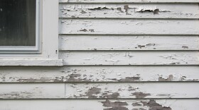 Peeling white paint on a calpboard hose with part of window