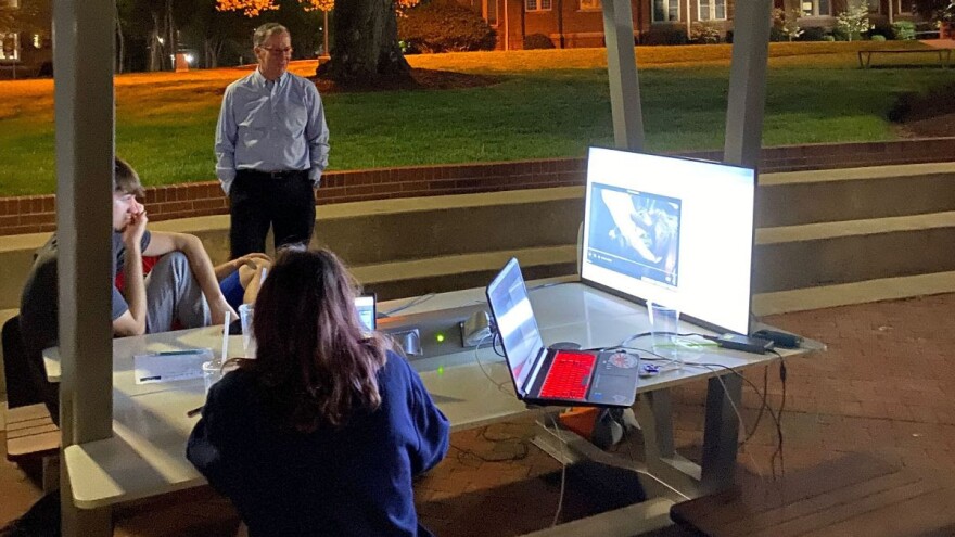 Brad Ives (standing) joins students watching TV at a new solar shelter in the plaza of the student union building.