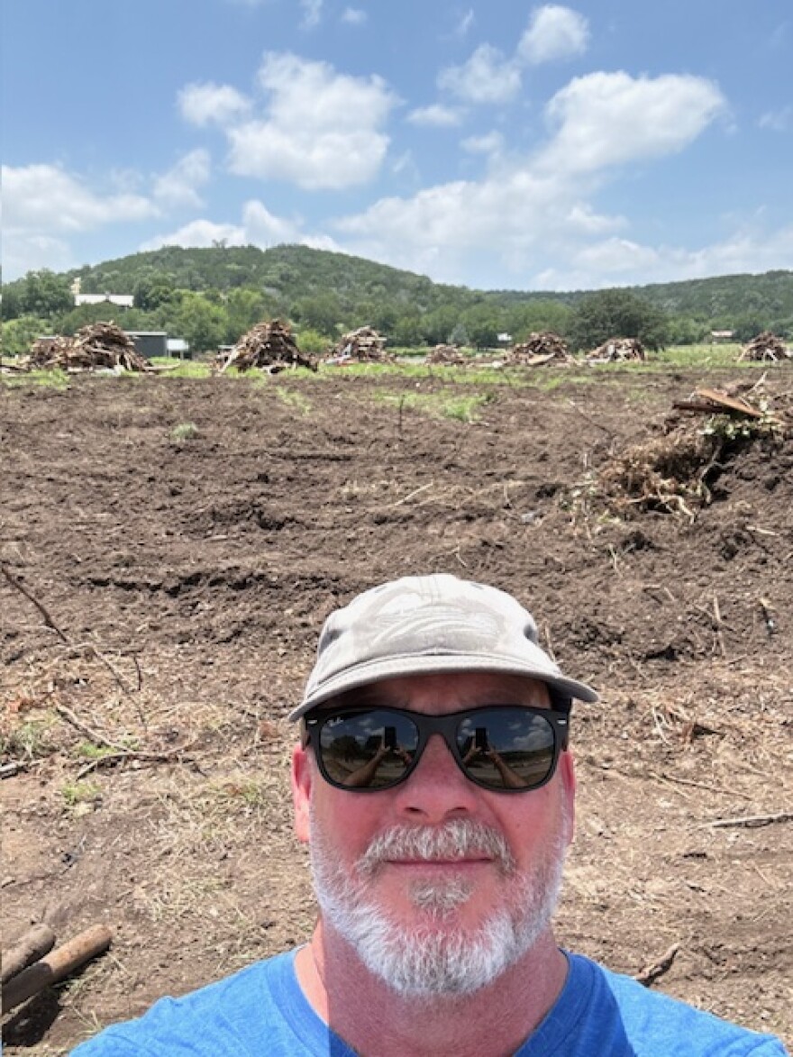 A man stands in front of a destroyed vineyard.