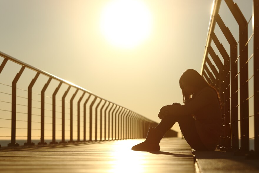 A teenage girl sits on a bridge at sunset.