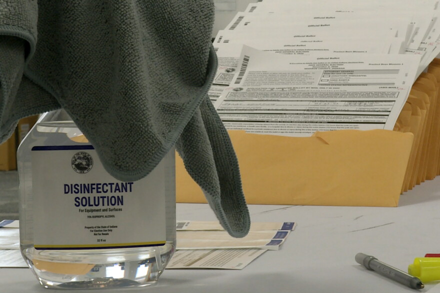 A stack of mail-in ballots to be sent out to voters, with a bottle of sanitizer nearby.