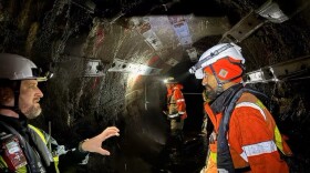 Men in heavy, orange reflective gear in a dark tunnel.