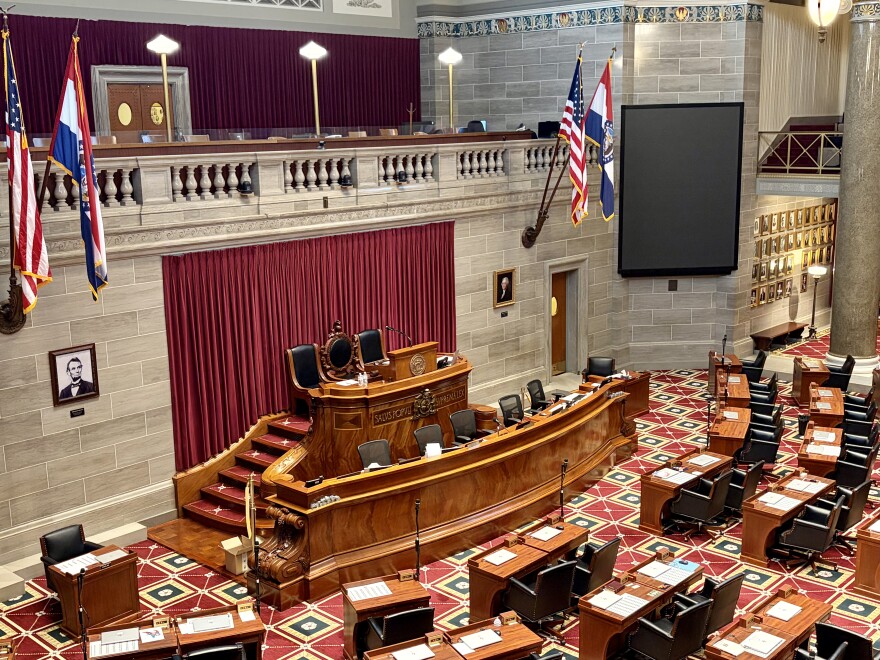 The wooden dais of the Missouri House of Representatives, as viewed from the upper gallery. American and Missouri flags hang from each side. 
