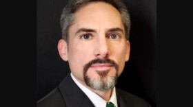 Head shot of man with a goatee and wearing a black suit with green spotted tie 