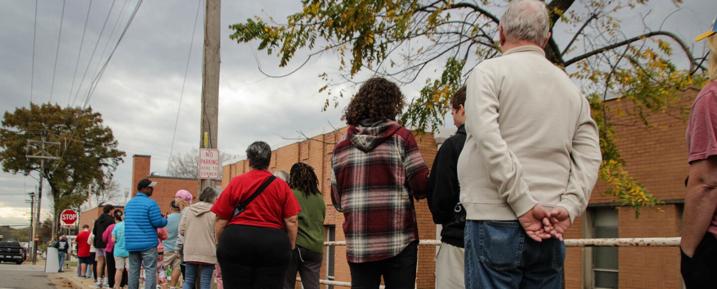 People wait in a line that stretches down the sidewalk. 