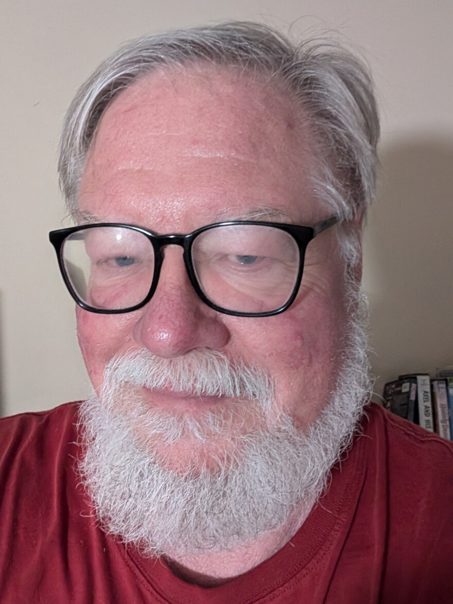 Close-up of a man in a red shirt, black framed glasses and a white beard